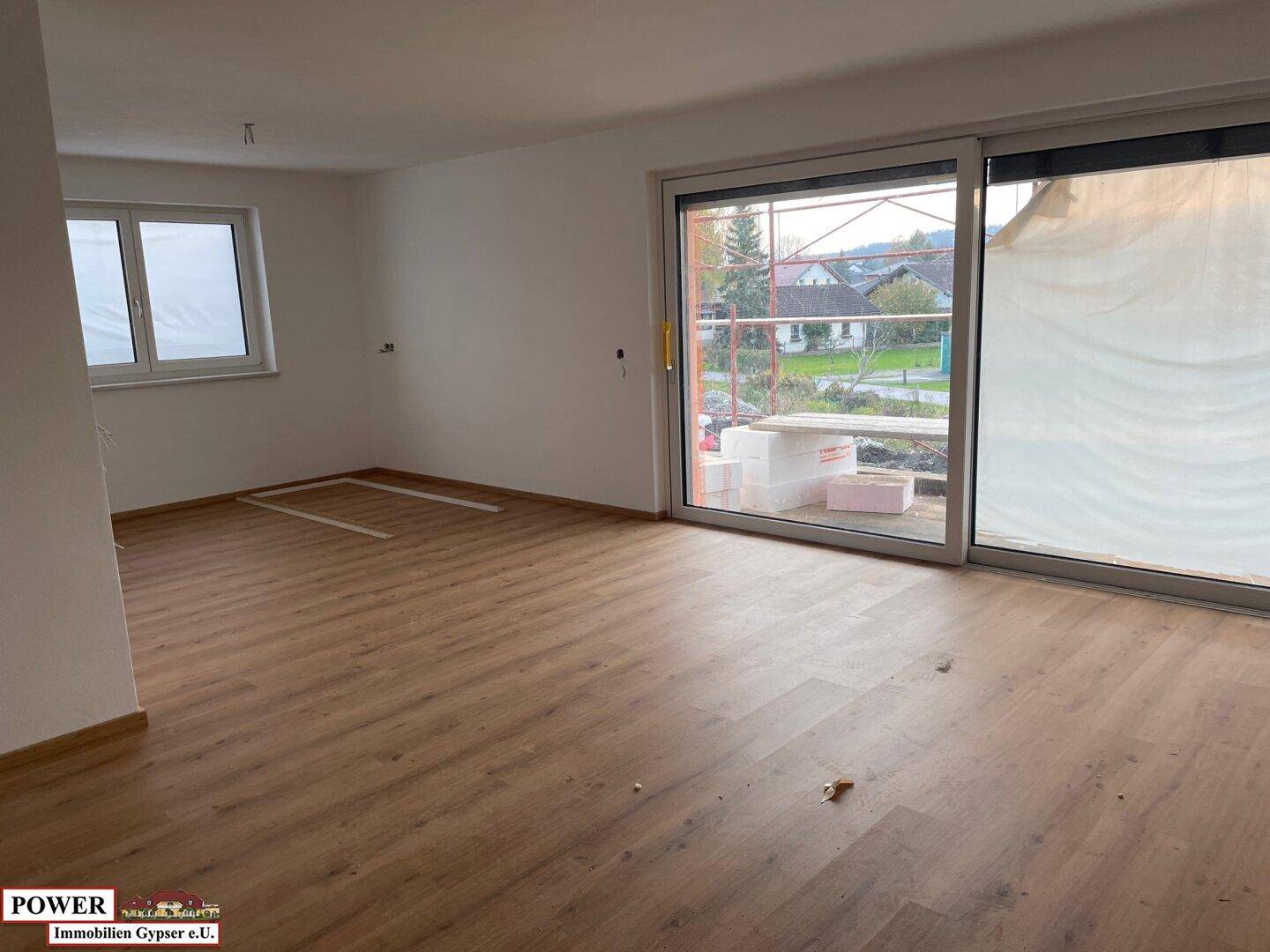 Lichtdurchflutetes Wohnzimmer mit Laminatboden und breiter Schiebetür zum Garten oder Balkon.