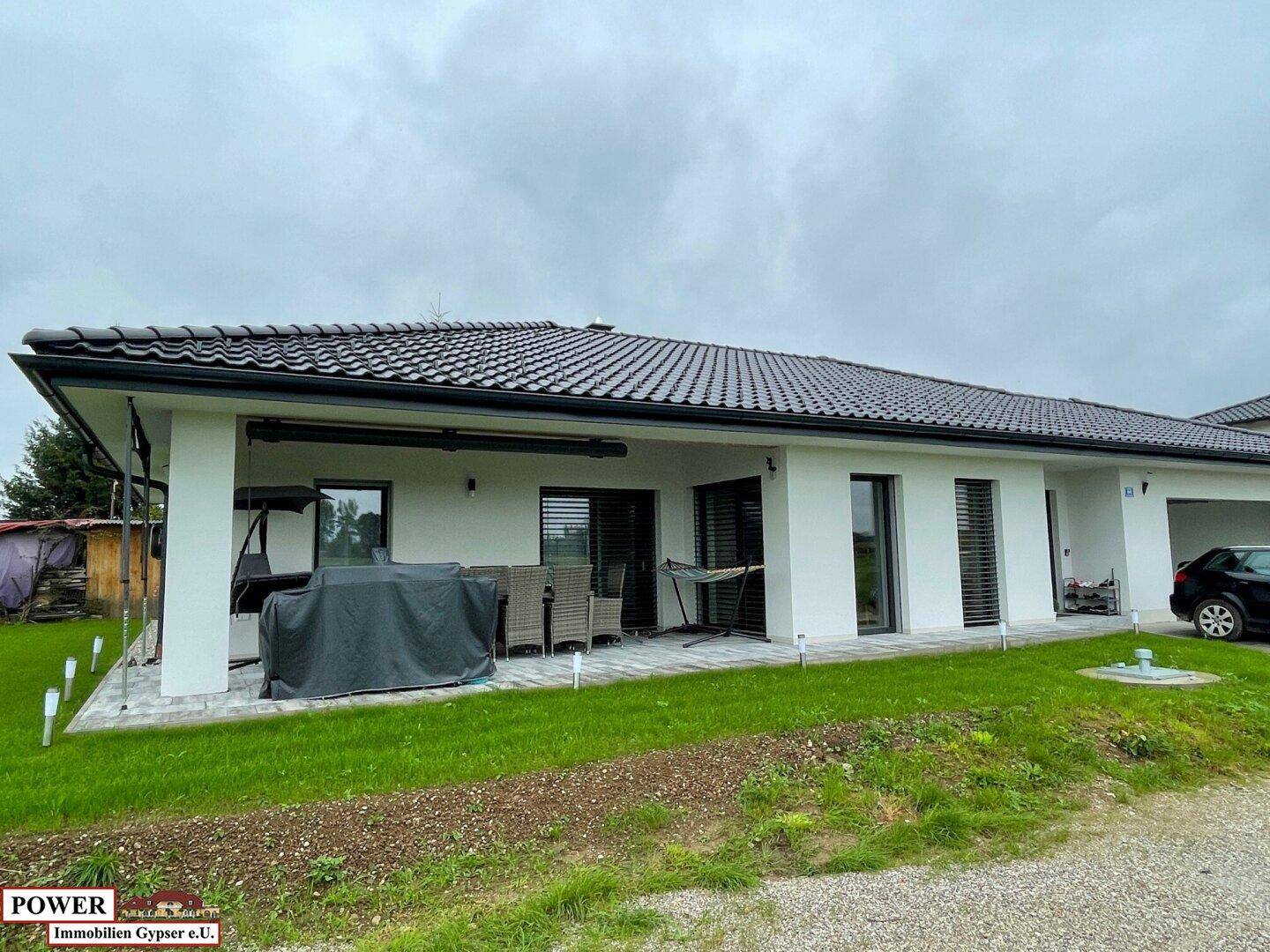 Geräumige überdachte Terrasse mit Schaukel und Grillbereich, angrenzend an eine Rasenfläche.