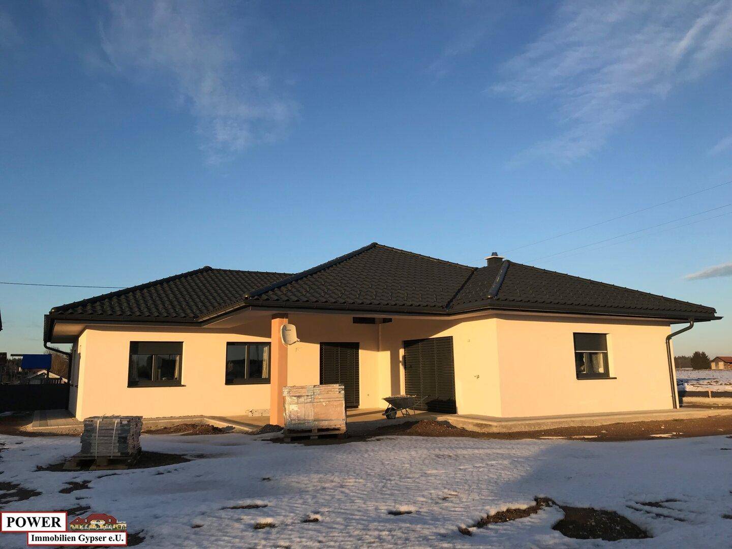 Fast fertiggestelltes Einfamilienhaus mit heller Fassade und dunklem Dach im Winter.