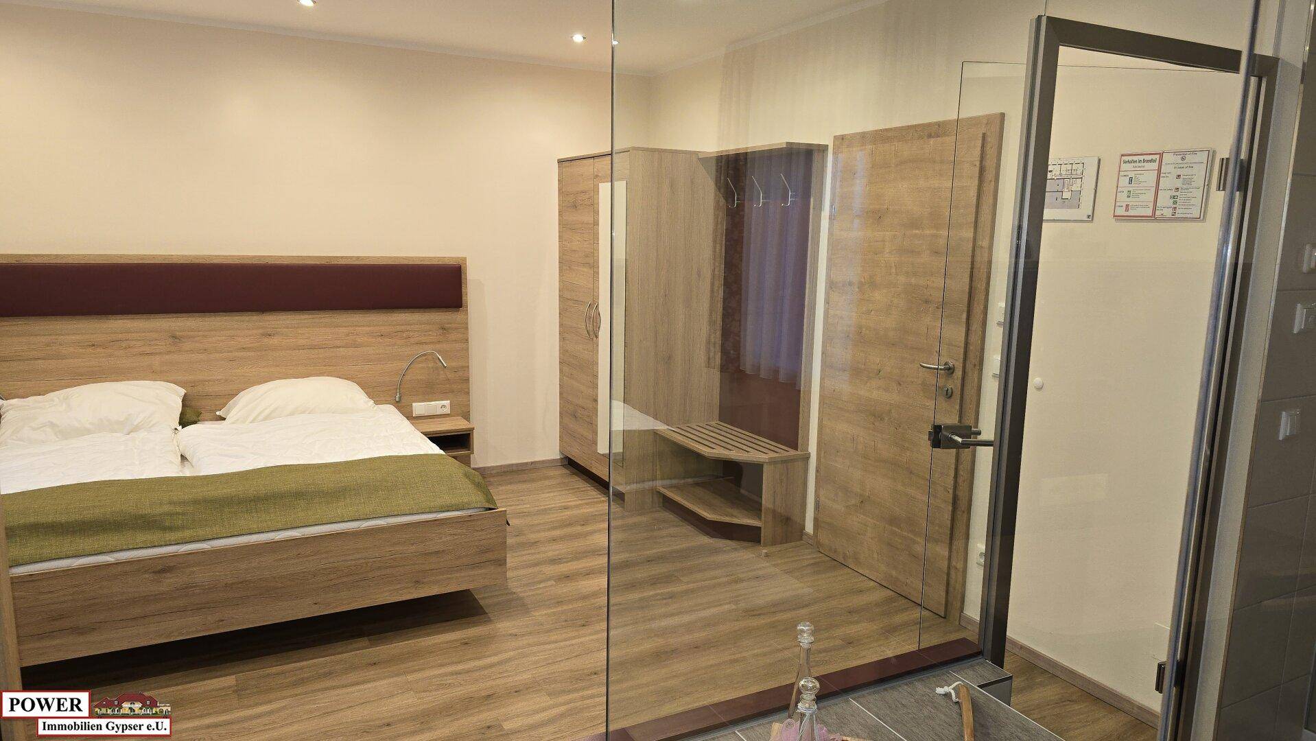 Modernes Schlafzimmer mit Holzbett, Kleiderschrank und Glaswand zum Bad.