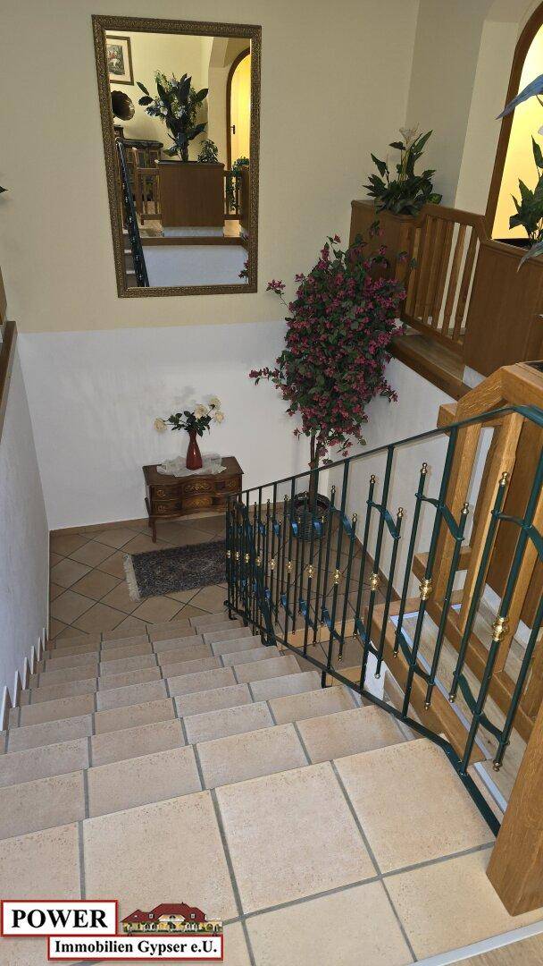 Helles Treppenhaus mit gefliesten Stufen, Holzgeländer und dekorativen Pflanzen.