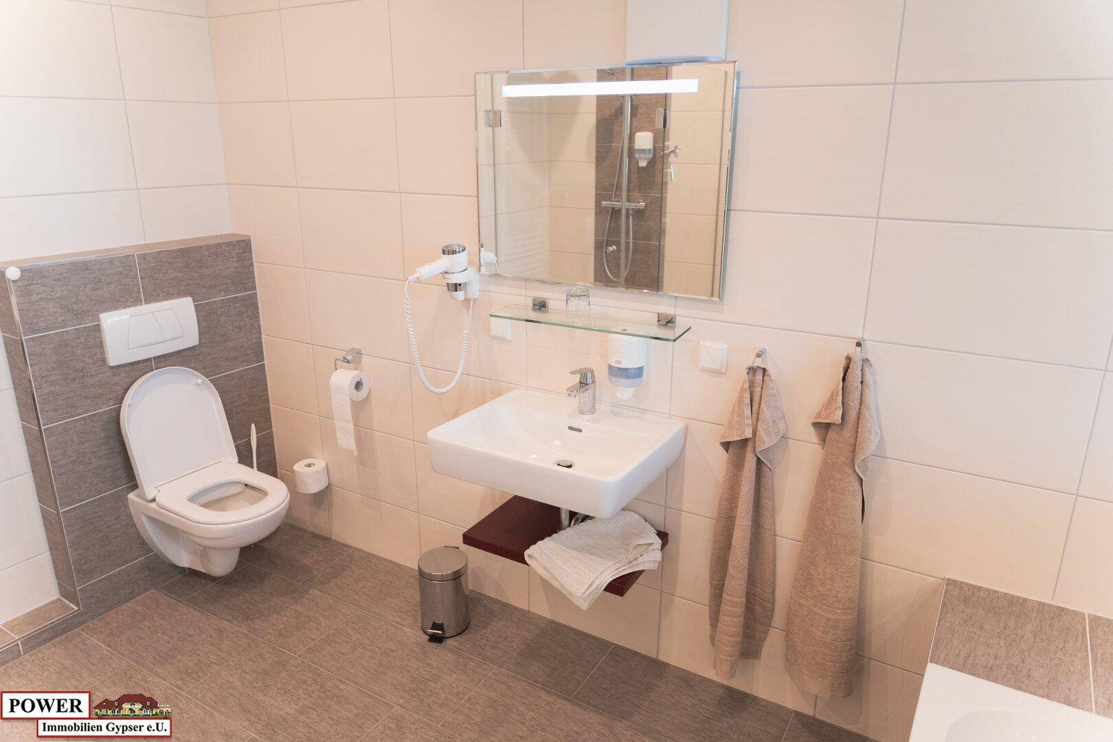 Helles Badezimmer mit wandhängendem WC, Waschbecken und großem Spiegel.