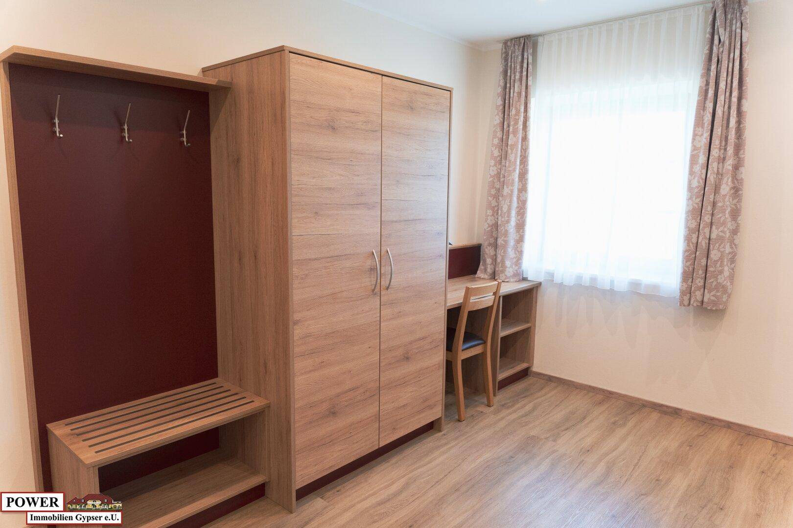 Helles Schlafzimmer mit Holzboden, Kleiderschrank, Schreibtisch und Fenster.