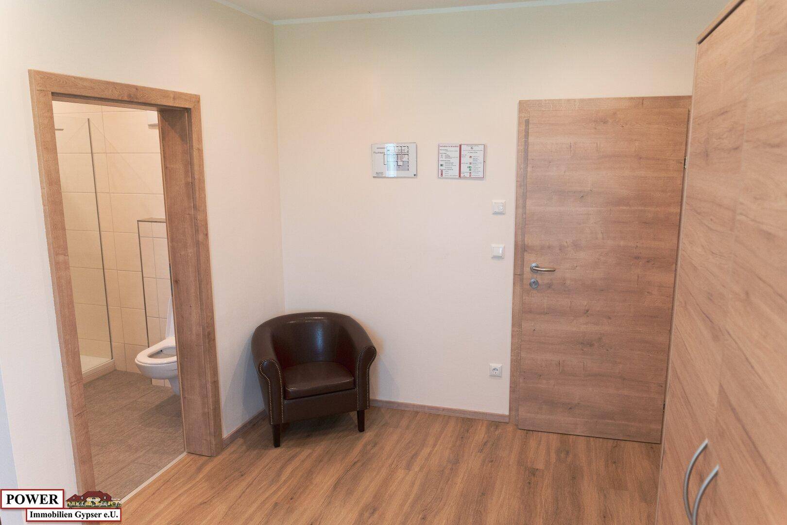 Schlafzimmer mit Holzboden, Sessel und Zugang zu einem modernen Badezimmer.