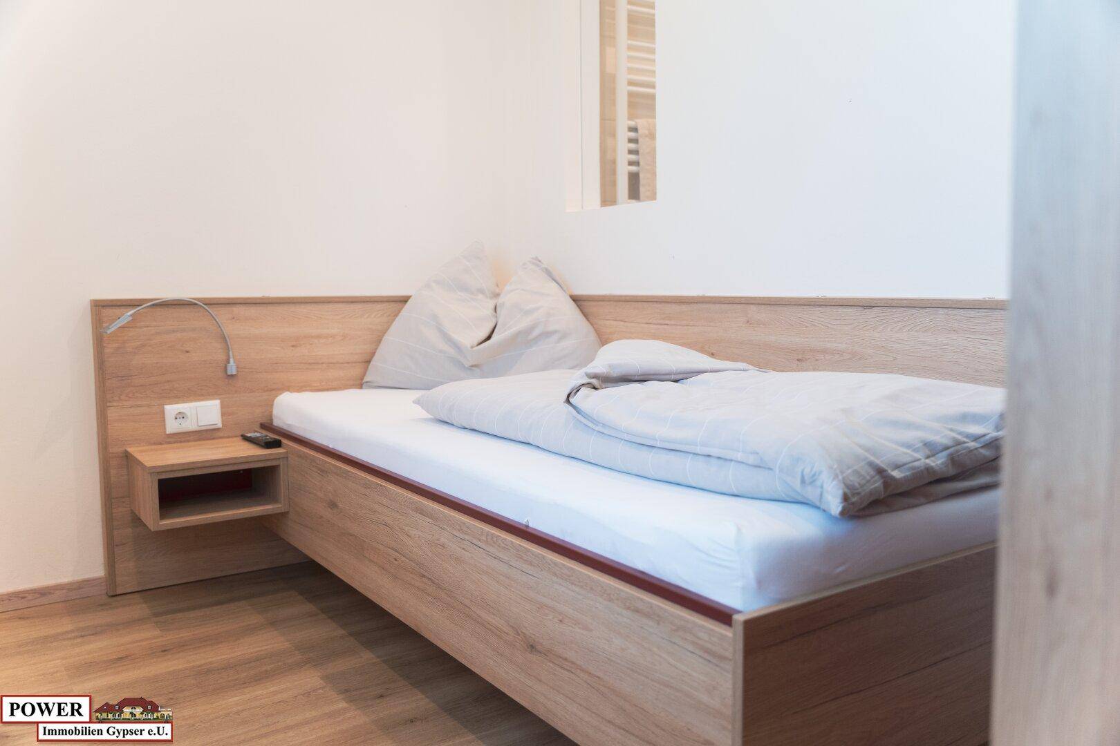 Einzelbett im Schlafzimmer mit Holzbettrahmen und Nachttischlampe.