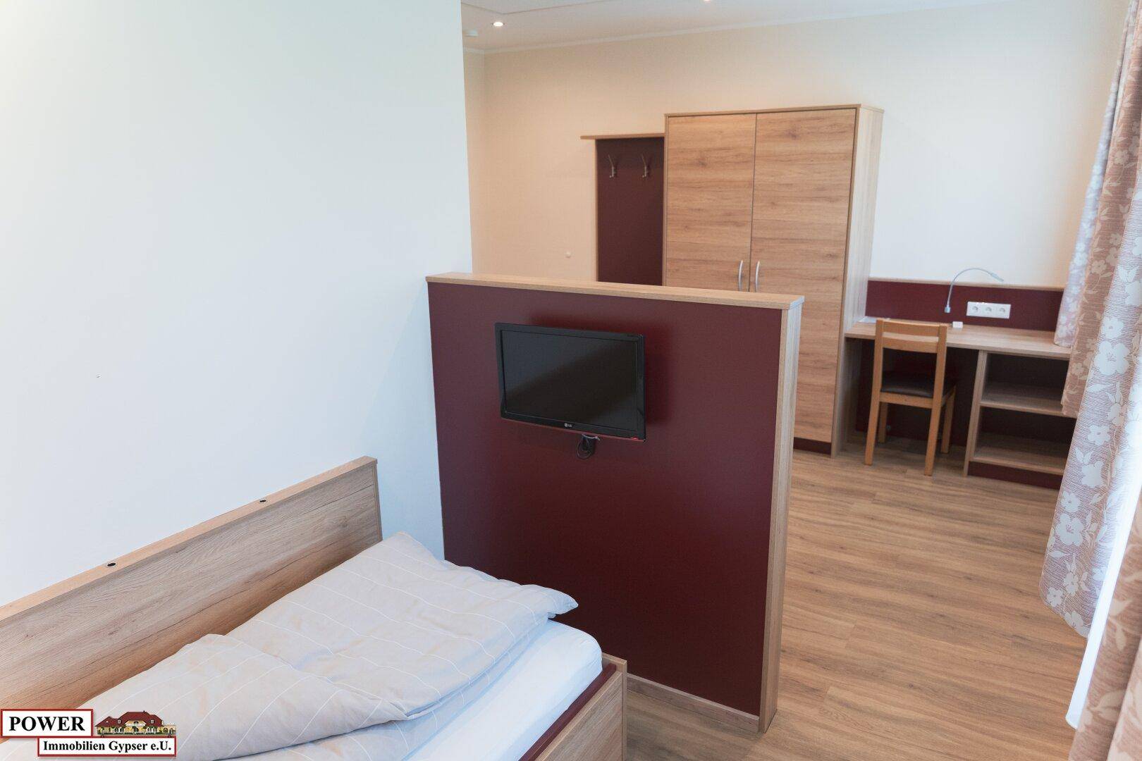 Schlafzimmer mit Einzelbett, Fernseher und Schreibtischbereich.