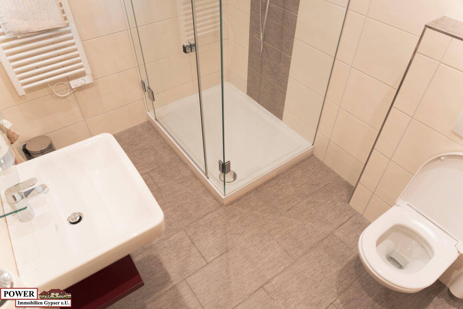 Helles Badezimmer mit Duschkabine, Waschbecken und wandhängendem WC.