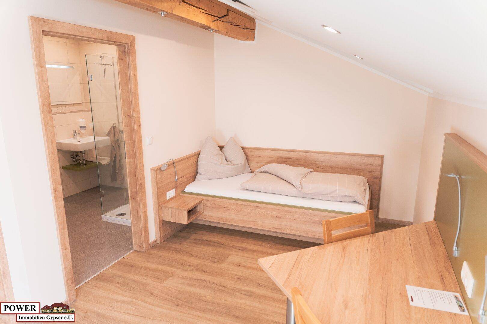 Schlafzimmer mit Einzelbett, Holzboden und direktem Zugang zum Badezimmer.