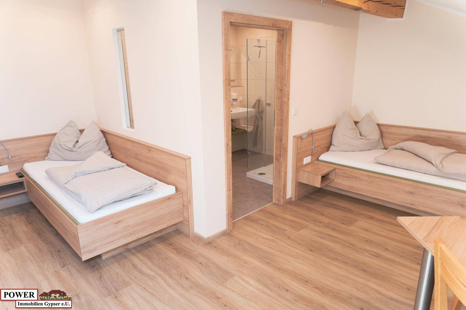 Schlafzimmer mit zwei Einzelbetten, Holzboden und Zugang zum Badezimmer.