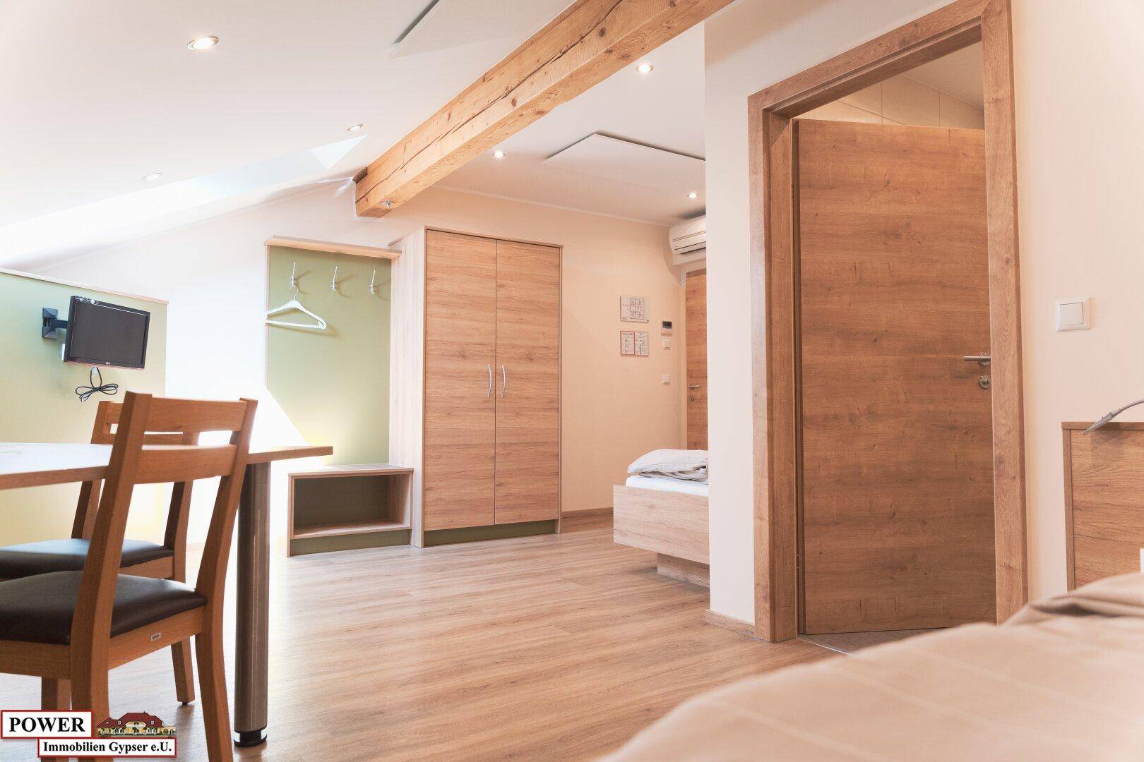 Schlafzimmer mit Holzboden, Kleiderschrank, Schreibtisch und Holzbalken an der Decke.