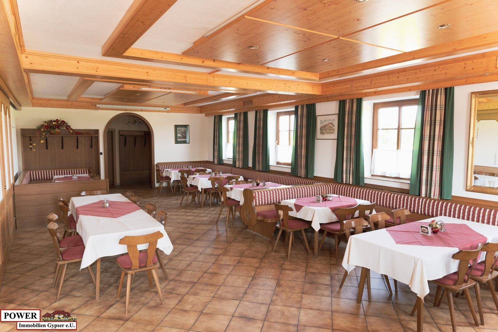 Heller Speisesaal mit traditioneller Einrichtung, Holzbalkendecke und Blick nach draußen.