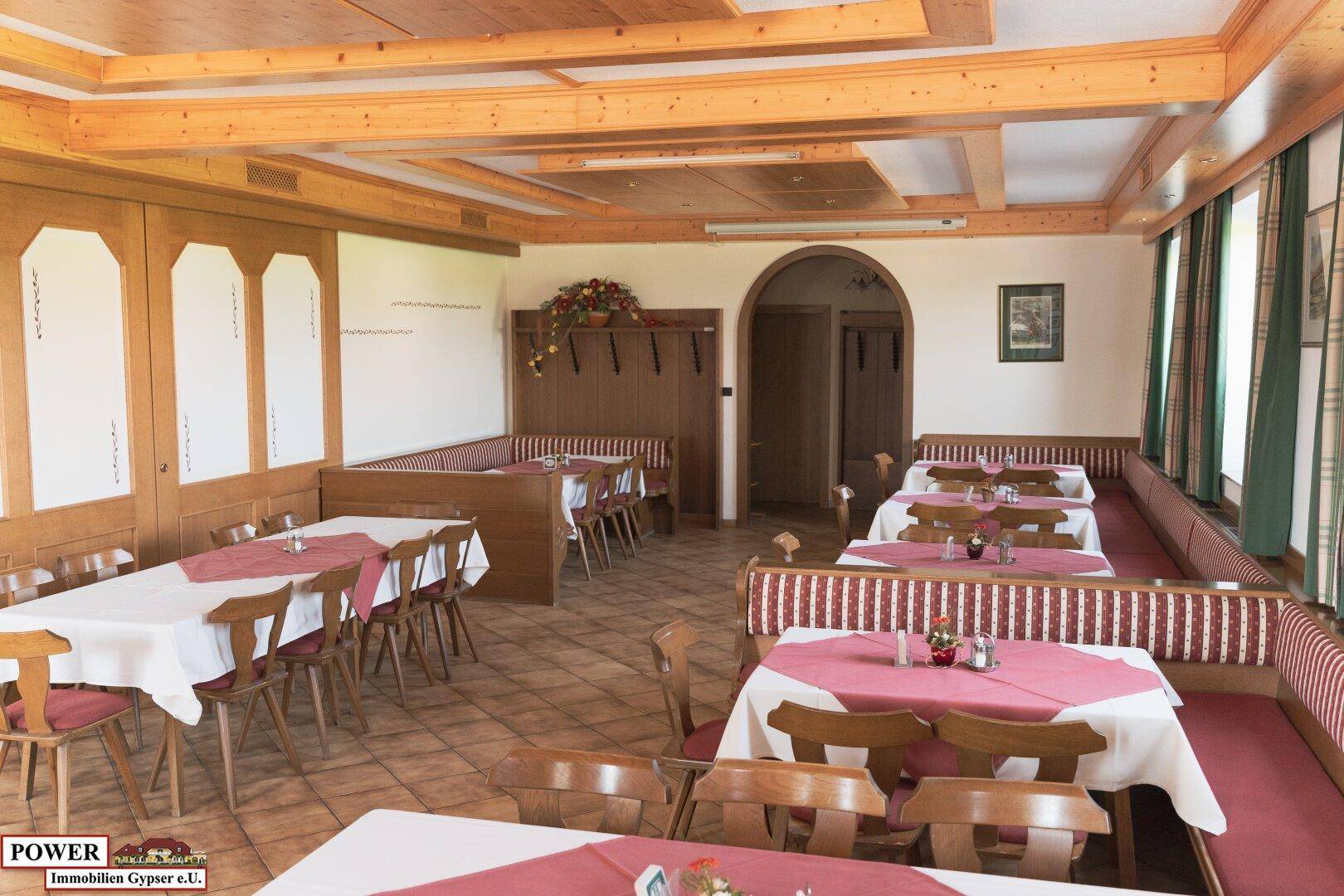 Gemütlicher Speisesaal mit Holztäfelung, karierten Bänken und mehreren Tischen für Gäste.
