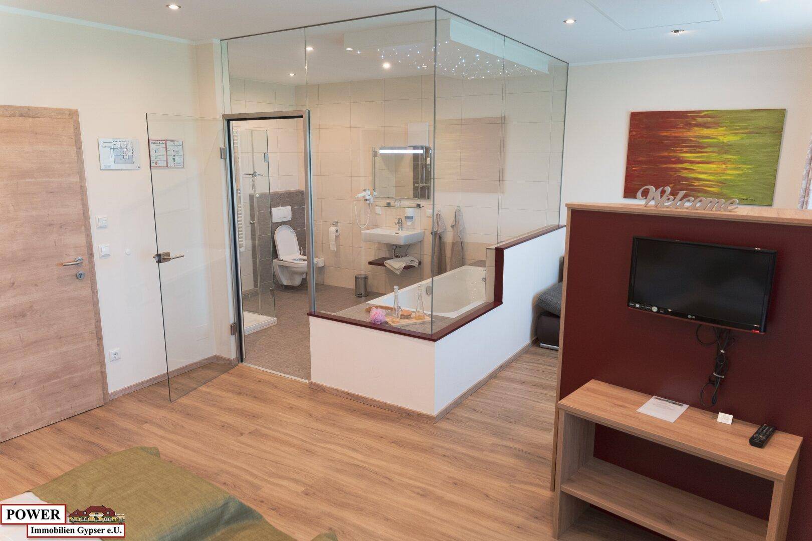Geräumiges Schlafzimmer mit integrierter Badewanne, Fernseher und Zugang zum Badezimmer.