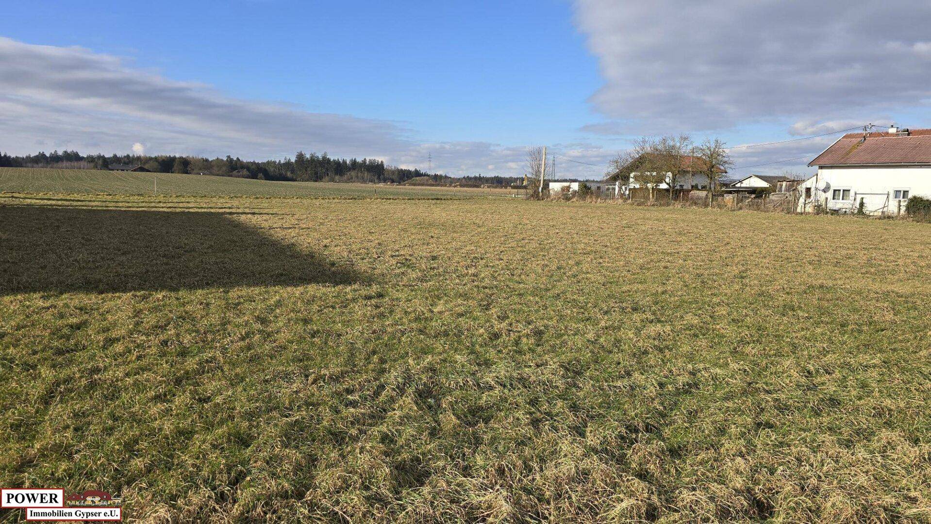 Offenes Feld mit Blick auf die ländliche Umgebung und einige Gebäude am Horizont unter hellem Himmel.