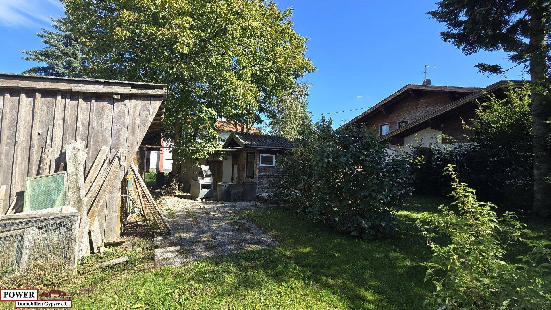 Gartenbereich mit Holzschuppen, einem kleinen Gartenhaus und üppiger Vegetation.