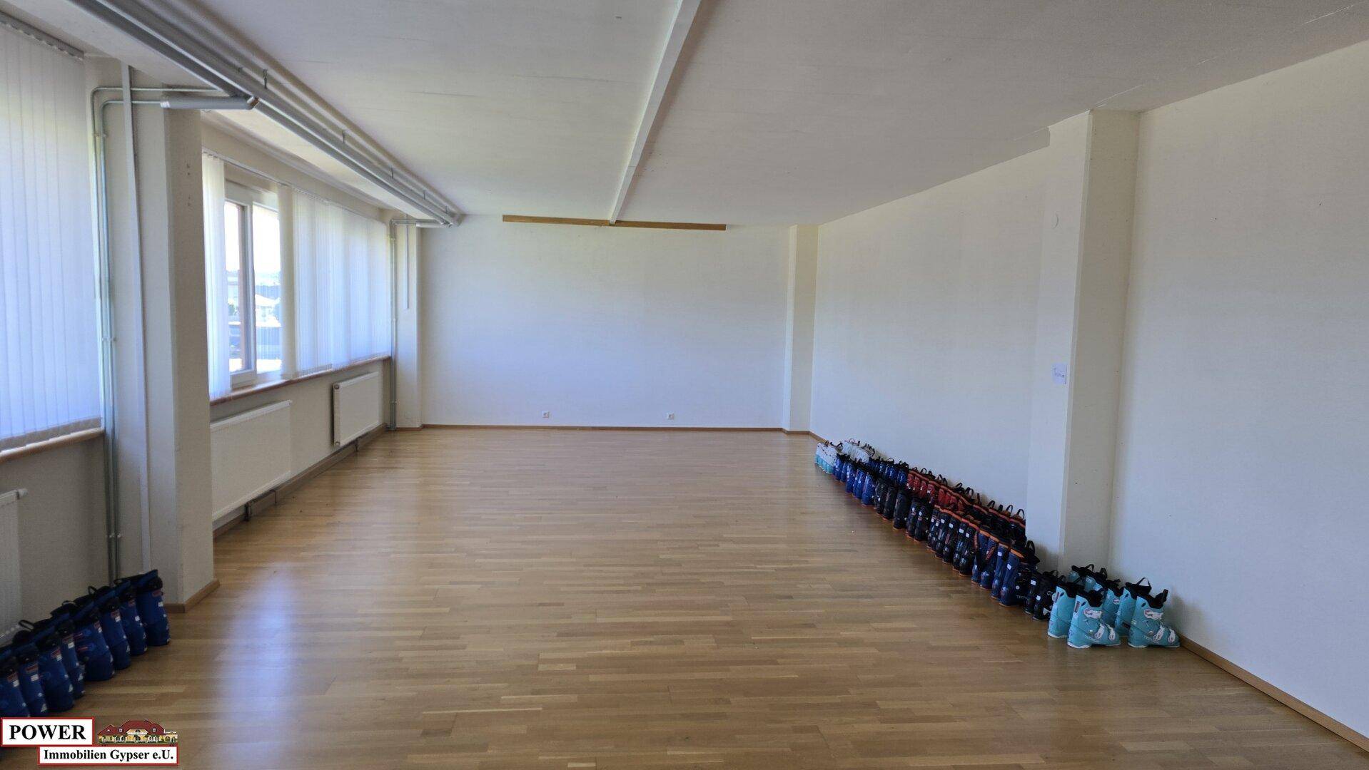 Großer, leerer Gewerberaum mit hellem Holzfußboden, großen Fenstern und guter Beleuchtung.