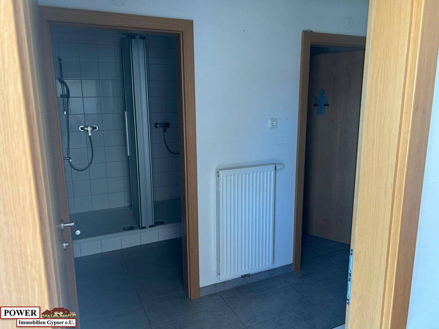 Funktionaler Badezimmerbereich mit Duschkabine, Fliesenboden und einem Heizkörper an der Wand.