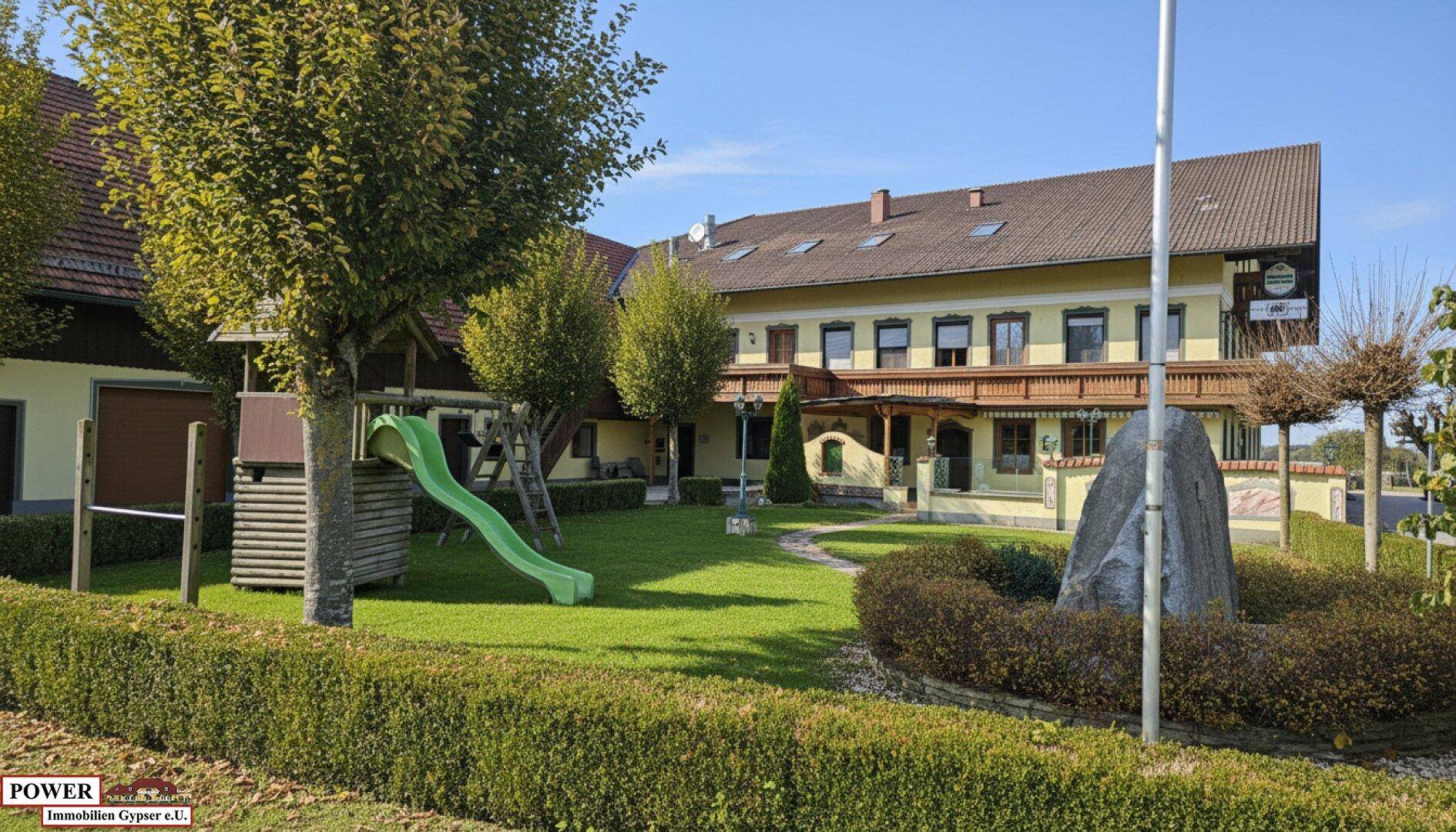 Sonniger Außenbereich mit Spielplatz und gepflegter Grünfläche vor dem traditionellen Gebäude.