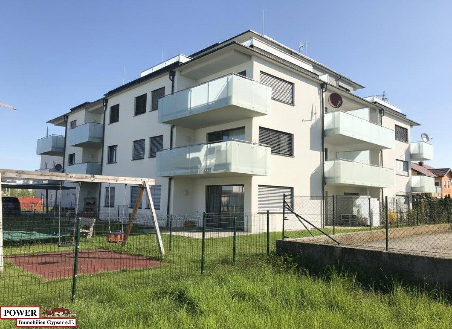 Neubau-Mehrfamilienhaus mit modernen Balkonen und einem Spielplatz im Vordergrund.