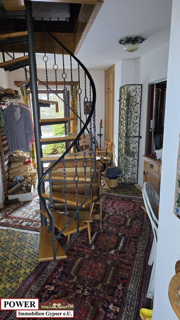 Elegante Wendeltreppe mit Holzstufen und schmiedeeisernem Geländer in einem Flurbereich.