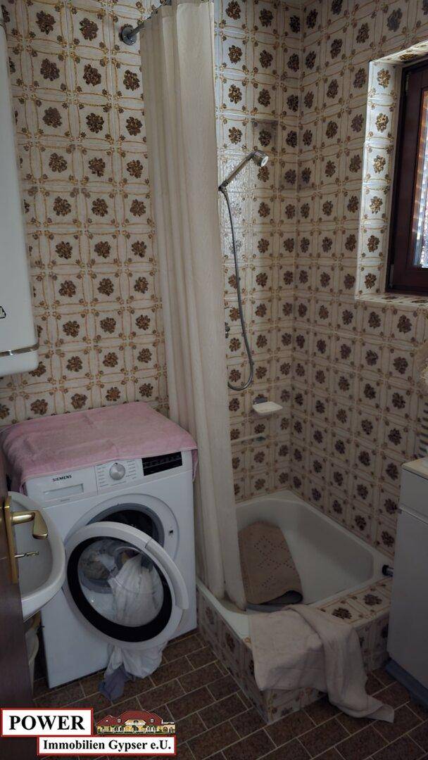 Badezimmer mit Duschwanne, Waschmaschine und traditionellen Fliesen an Wänden und Boden.