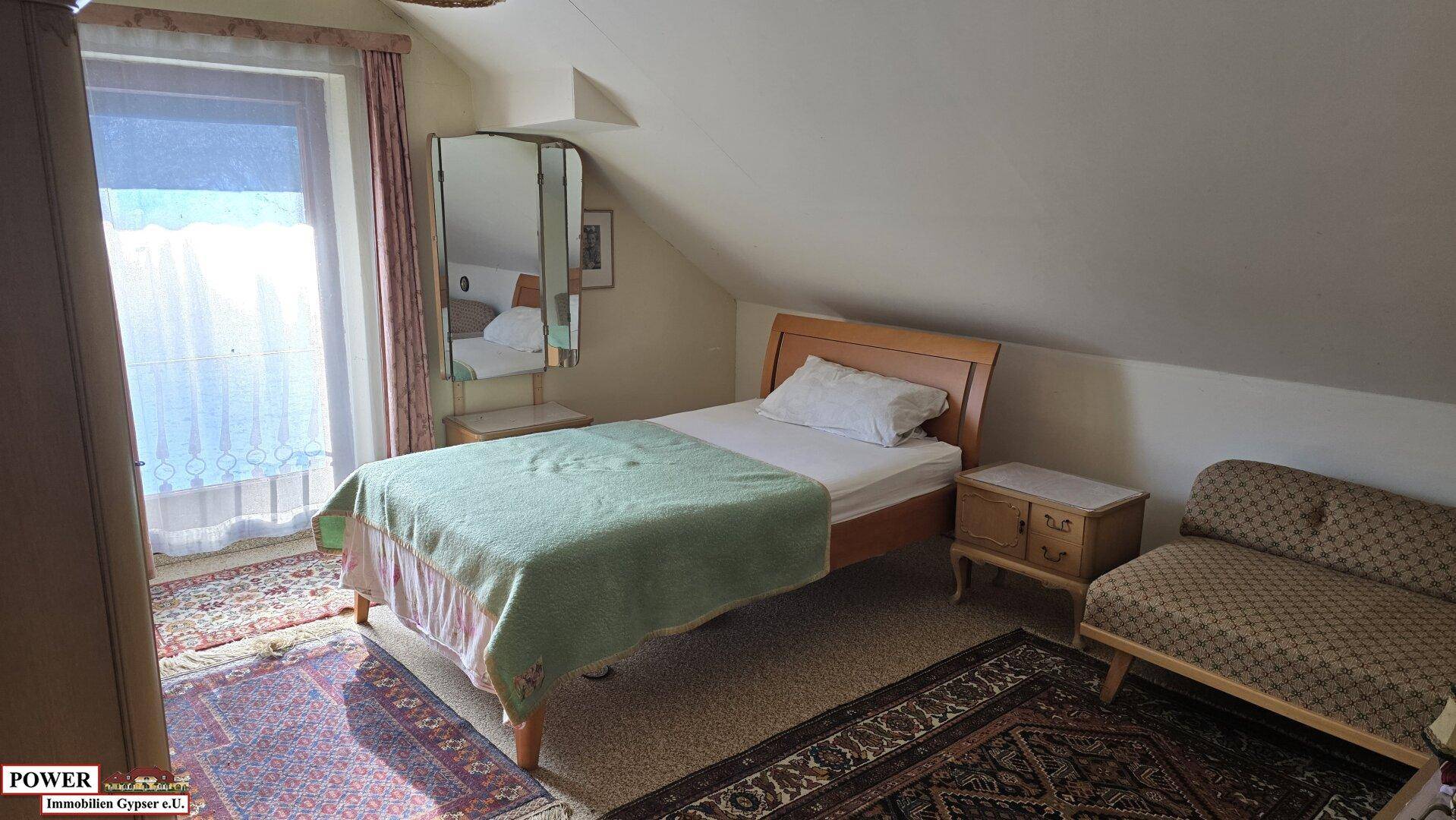 Gemütliches Schlafzimmer im Dachgeschoss mit schrägen Wänden und Teppichboden.