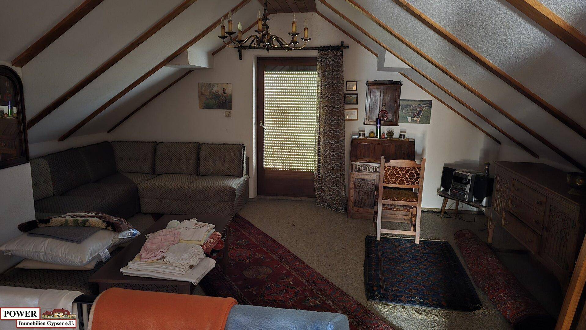 Geräumiges Wohnzimmer im Dachgeschoss mit schrägen Wänden und Zugang zum Balkon.