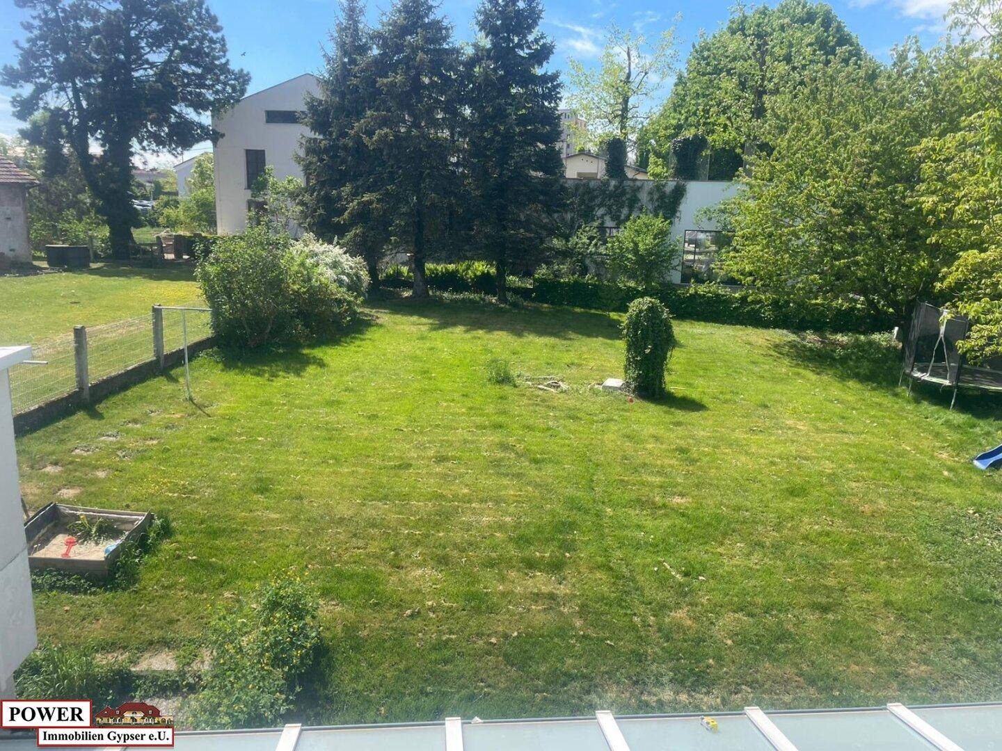 Weitläufiger Garten mit grüner Rasenfläche, hohen Bäumen und einem kleinen Spielbereich.
