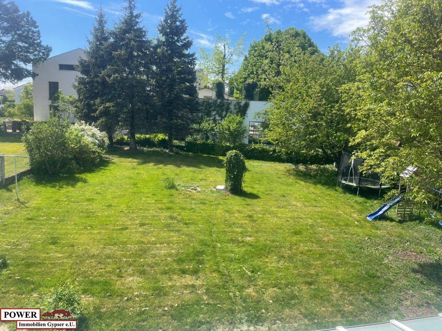 Großer, gepflegter Garten mit Rasenfläche, Bäumen und Kinderspielplatz im Hintergrund.
