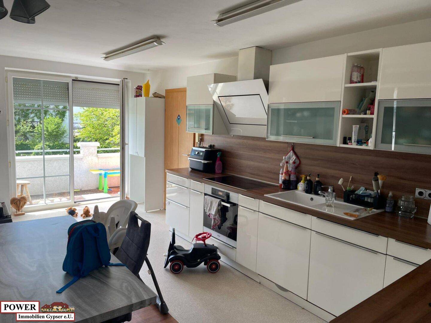 Moderne Küche mit weißen Hochglanzfronten, Holzarbeitsplatte und Zugang zum sonnigen Balkon.