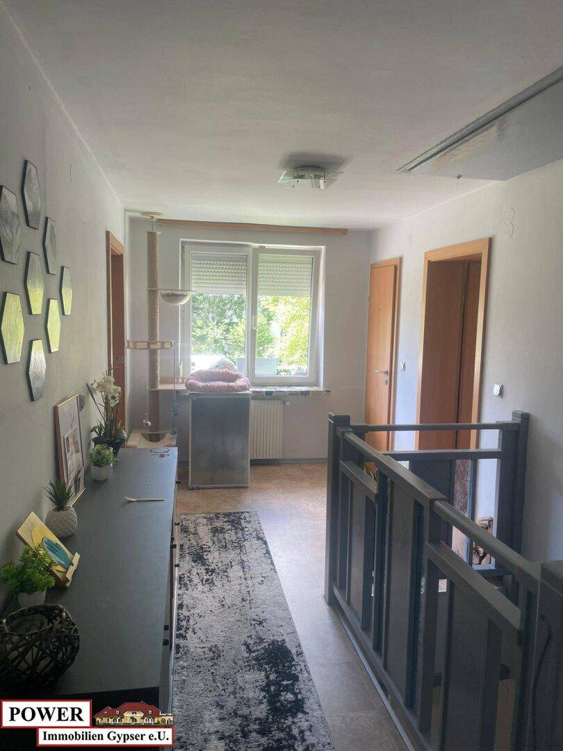 Heller Flur im Obergeschoss mit Fenster, Treppengeländer und dekorativen Wandelementen.