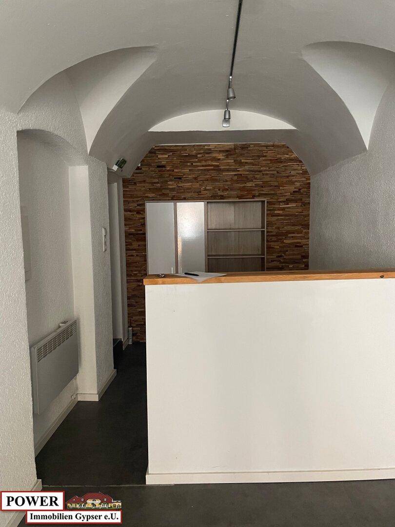 Innenansicht eines Geschäftsraums mit dekorativer Holzvertäfelung an der Rückwand und einer eleganten Gewölbedecke. Ein Heizkörper ist an der Wand montiert.