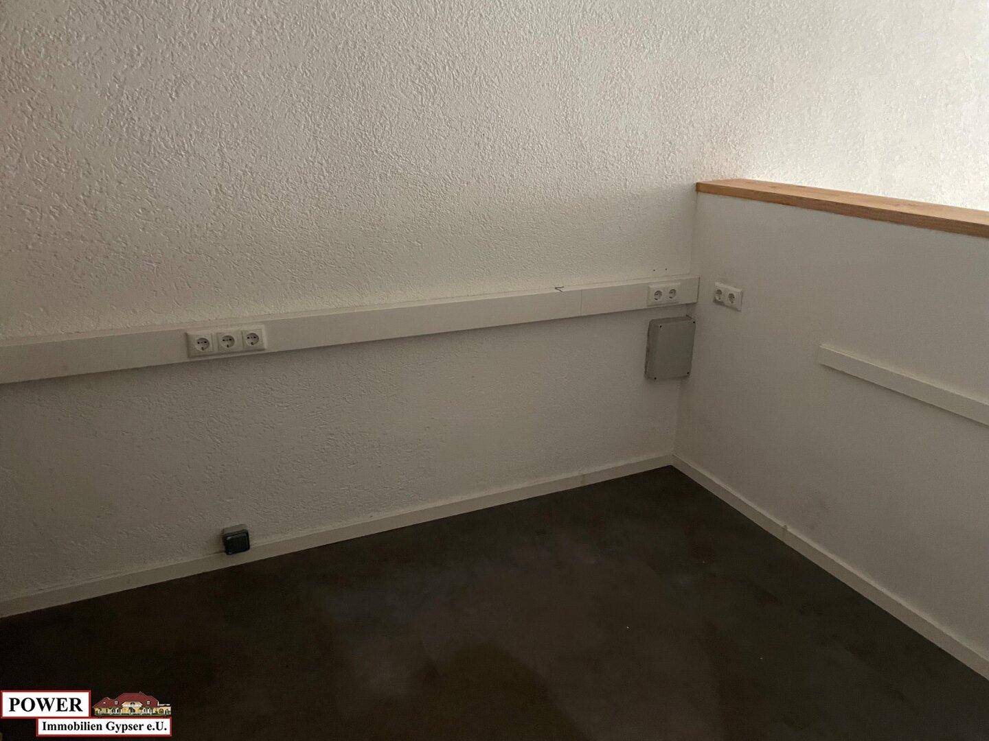 Detailansicht einer weißen Wand mit mehreren Steckdosenleisten und einem Heizkörper in einem Geschäftsraum. Der Boden ist dunkel.