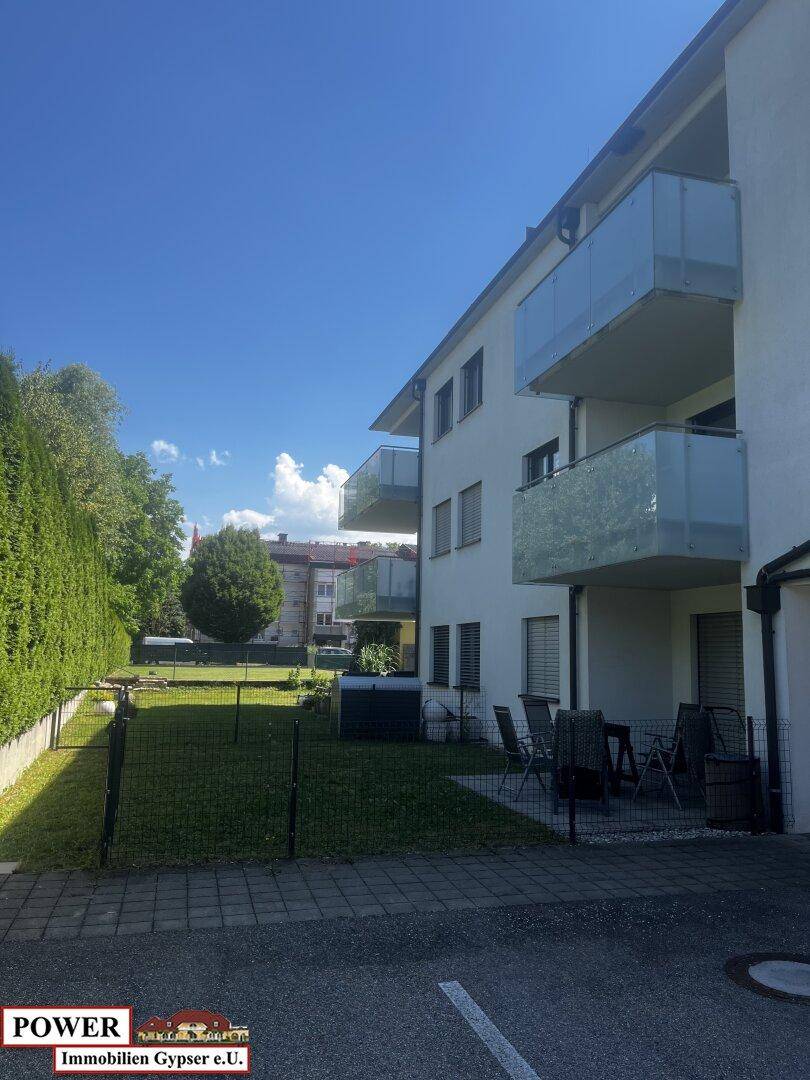 Außenansicht eines Wohngebäudes mit Balkonen und einem kleinen, gepflegten Gartenbereich.