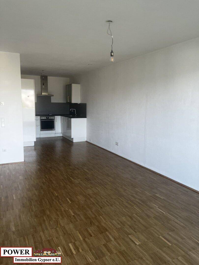 Offener Küchenbereich mit weißen Schränken und Holzboden, Teil eines größeren Wohnraums.