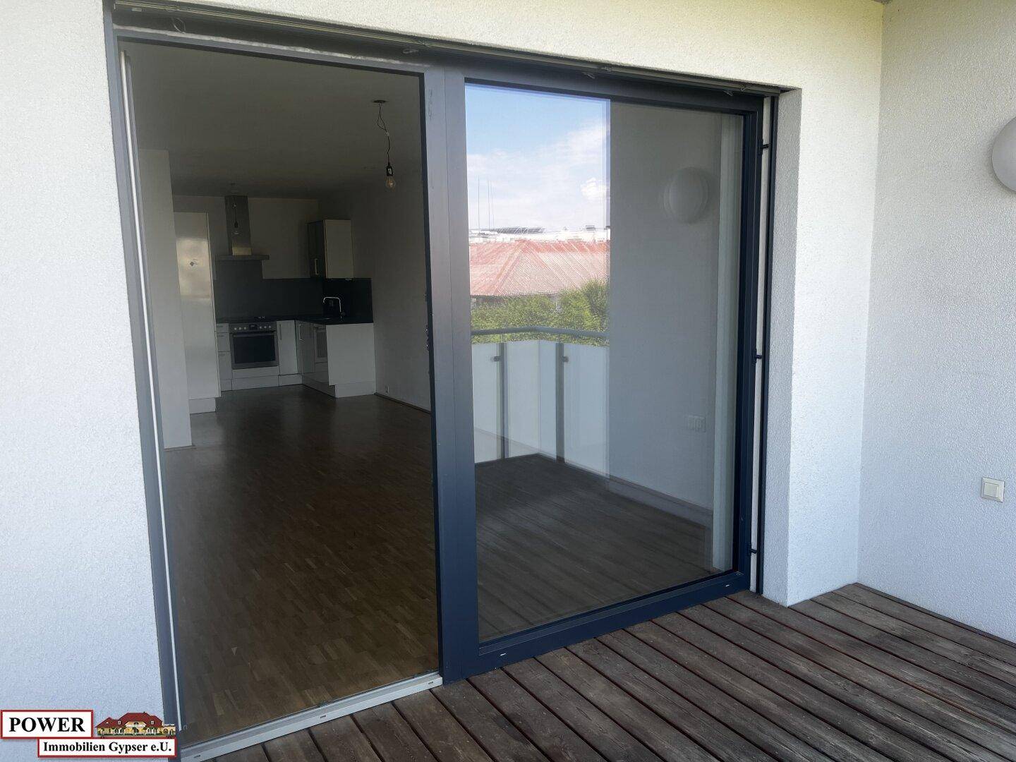 Blick vom Balkon in den Innenraum mit sichtbarer Küche und Holzdielen auf dem Balkon.