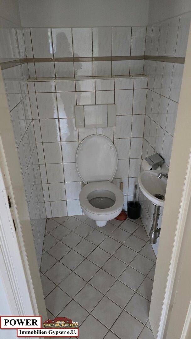 Funktionales Gäste-WC mit Fliesenboden, wandhängender Toilette und kleinem Waschbecken.
