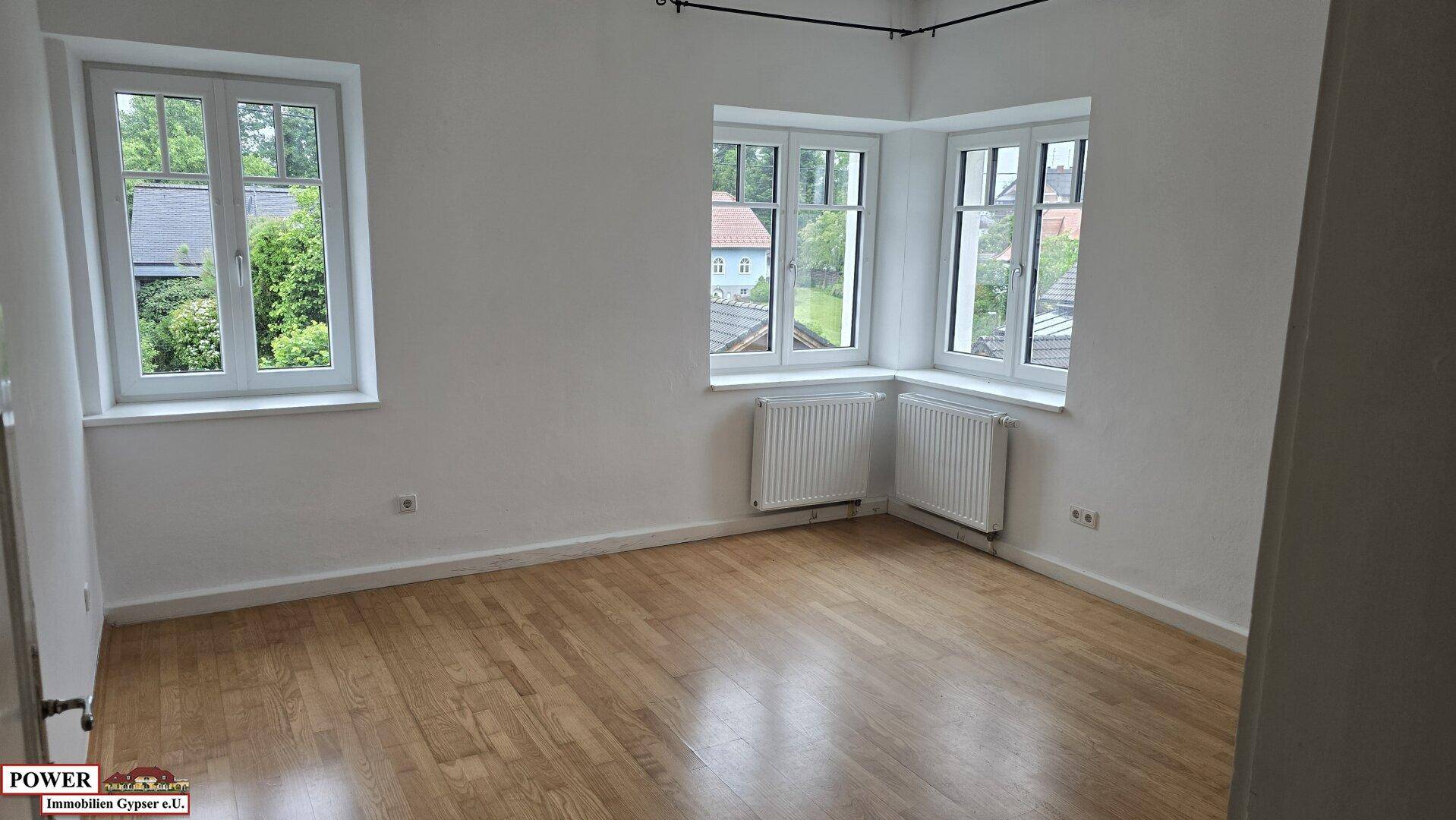 Geräumiges Zimmer mit Eichenparkett und großen Fenstern, die einen Blick ins Grüne ermöglichen.
