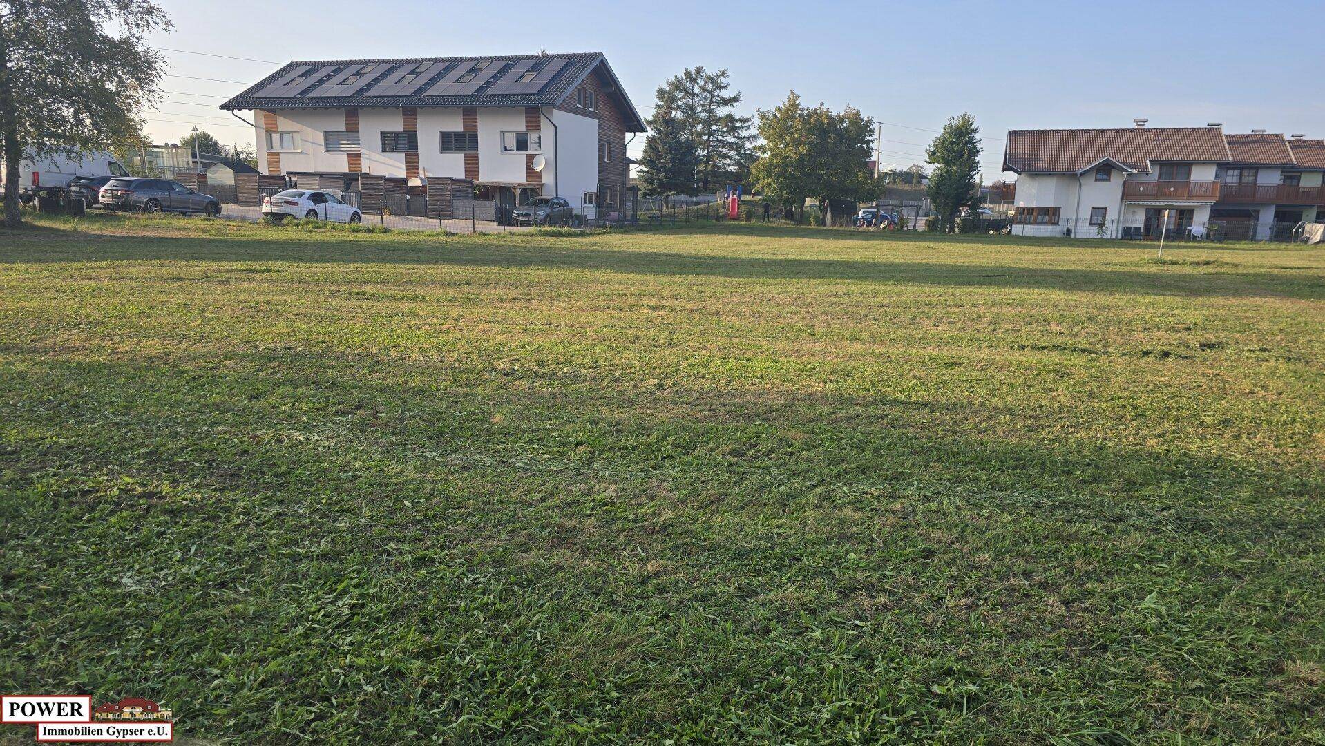 Ausgedehnte Rasenfläche mit modernen Wohnhäusern und Bäumen im Hintergrund bei Tageslicht.
