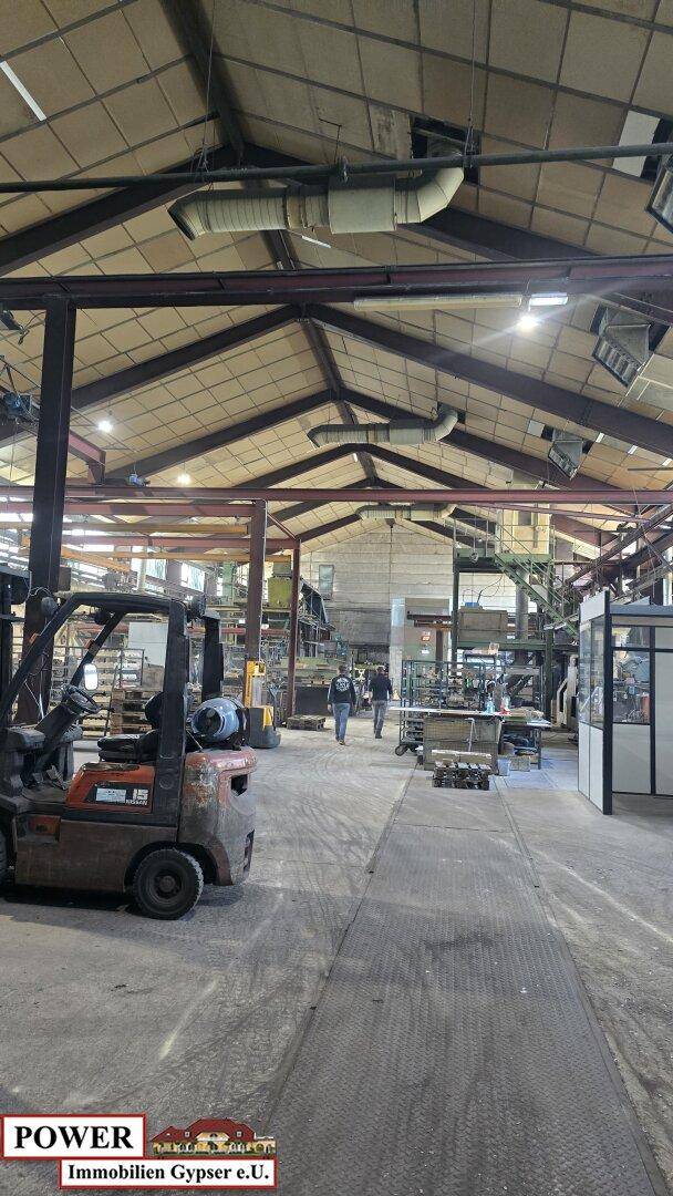 Geräumige Industriehalle mit hohen Decken, sichtbaren Stahlträgern und Gabelstaplern auf dem Betonboden.
