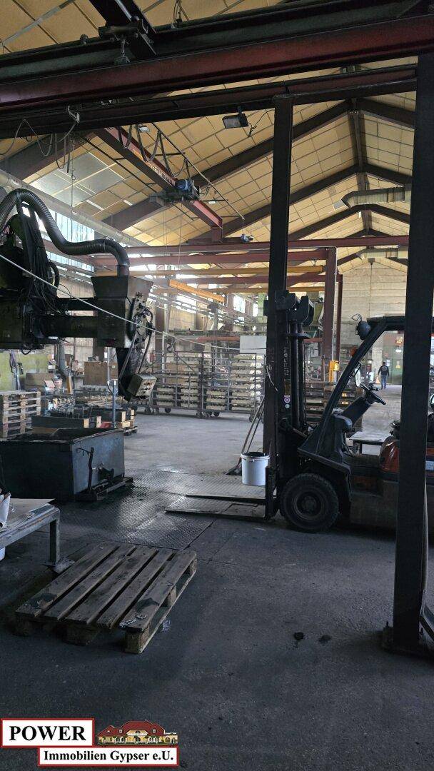 Innenansicht einer großen Industriehalle mit Maschinen, Paletten und einem Gabelstapler auf dem Boden.
