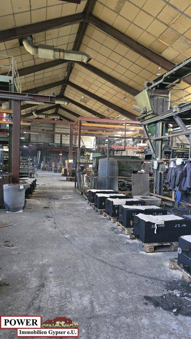 Weitläufige Industriehalle mit Produktionsanlagen, hohen Decken und einem robusten Betonboden.