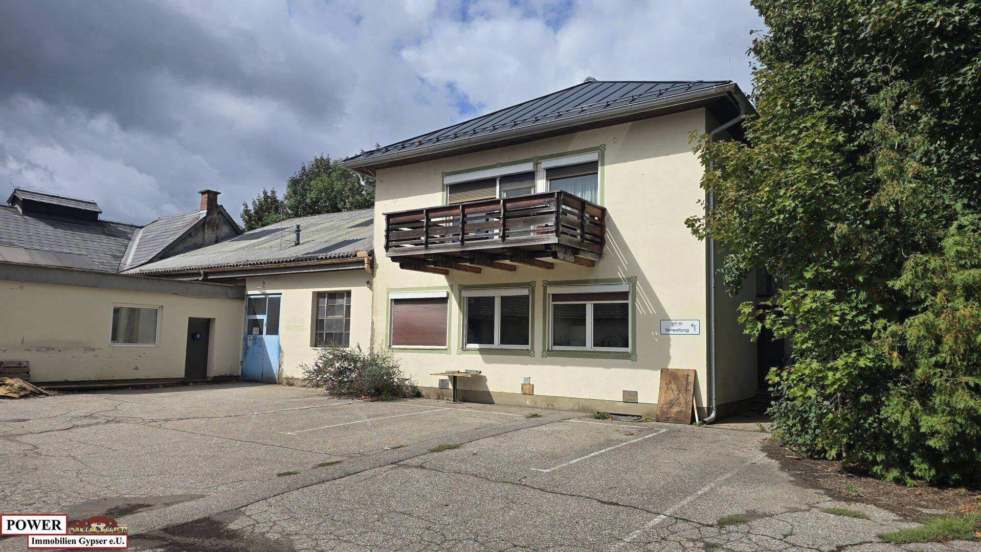 Nahaufnahme eines Gebäudes mit einem kleinen Holzbalkon und mehreren Fenstern, umgeben von Bäumen.