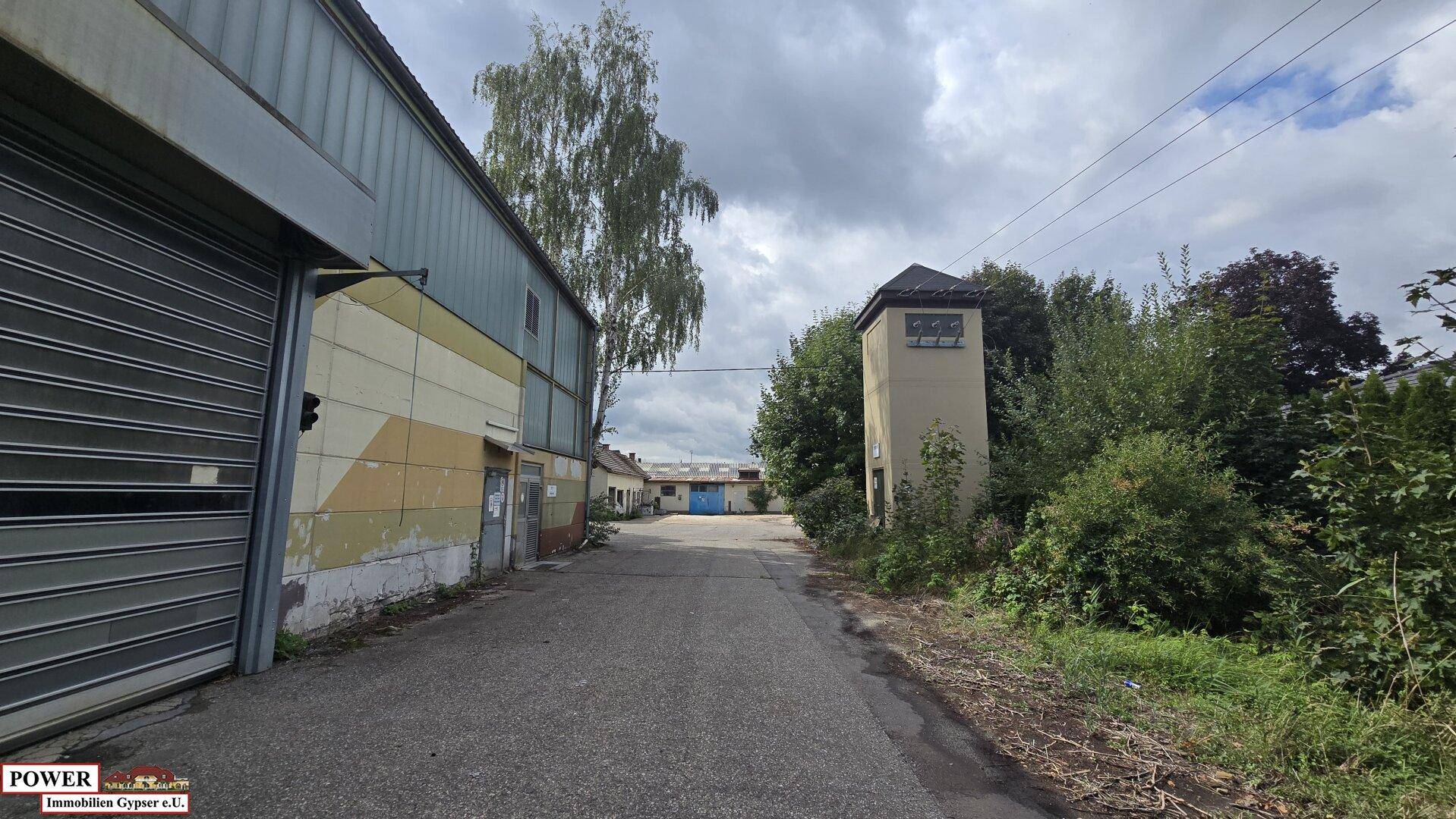 Zufahrtsweg zu einem Industrieareal mit einem kleinen Turm und verschiedenen Gebäuden im Hintergrund.