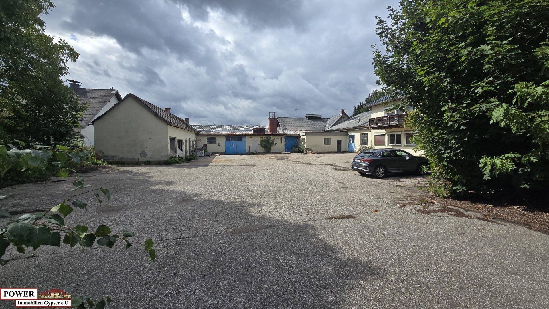 Gesamtansicht des Gewerbeareals mit mehreren Gebäuden und einem weitläufigen Parkplatz, umgeben von Bäumen.