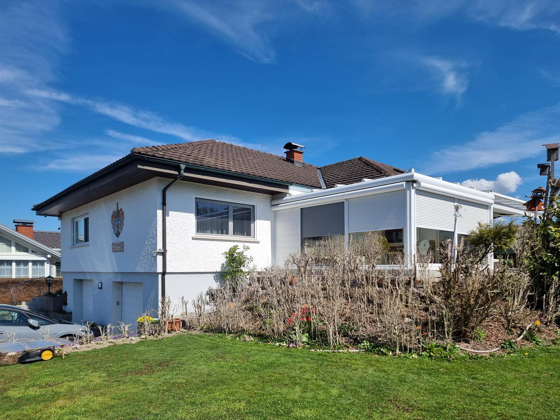 Seitenansicht des Hauses mit Wintergarten und gepflegtem Gartenbereich.