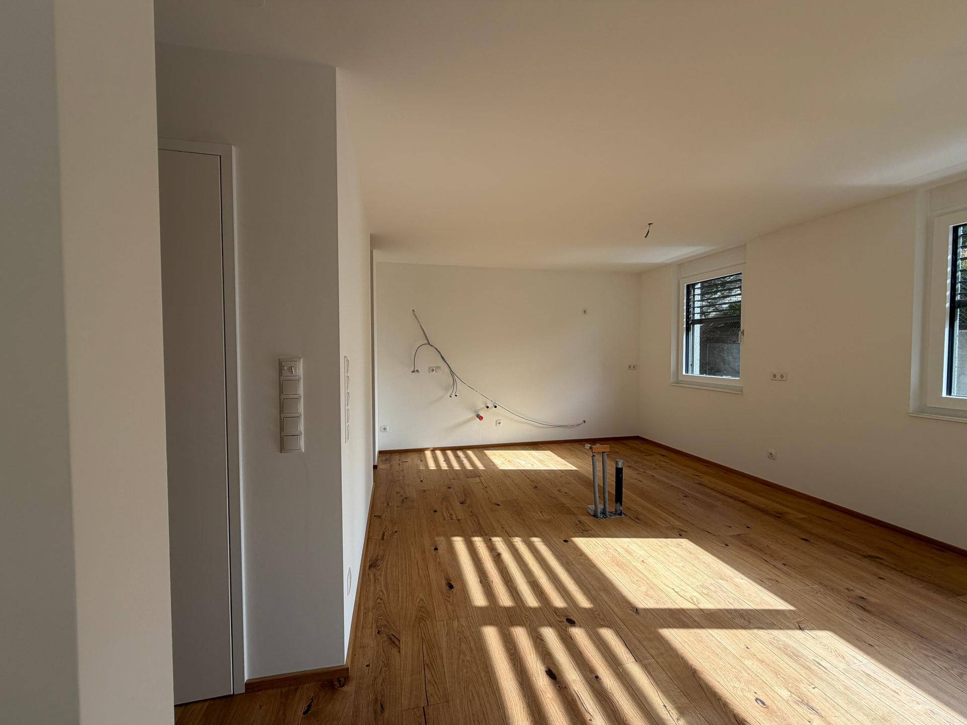 Heller, unmöblierter Raum mit Holzboden und großen Fenstern, bereit für die Einrichtung.