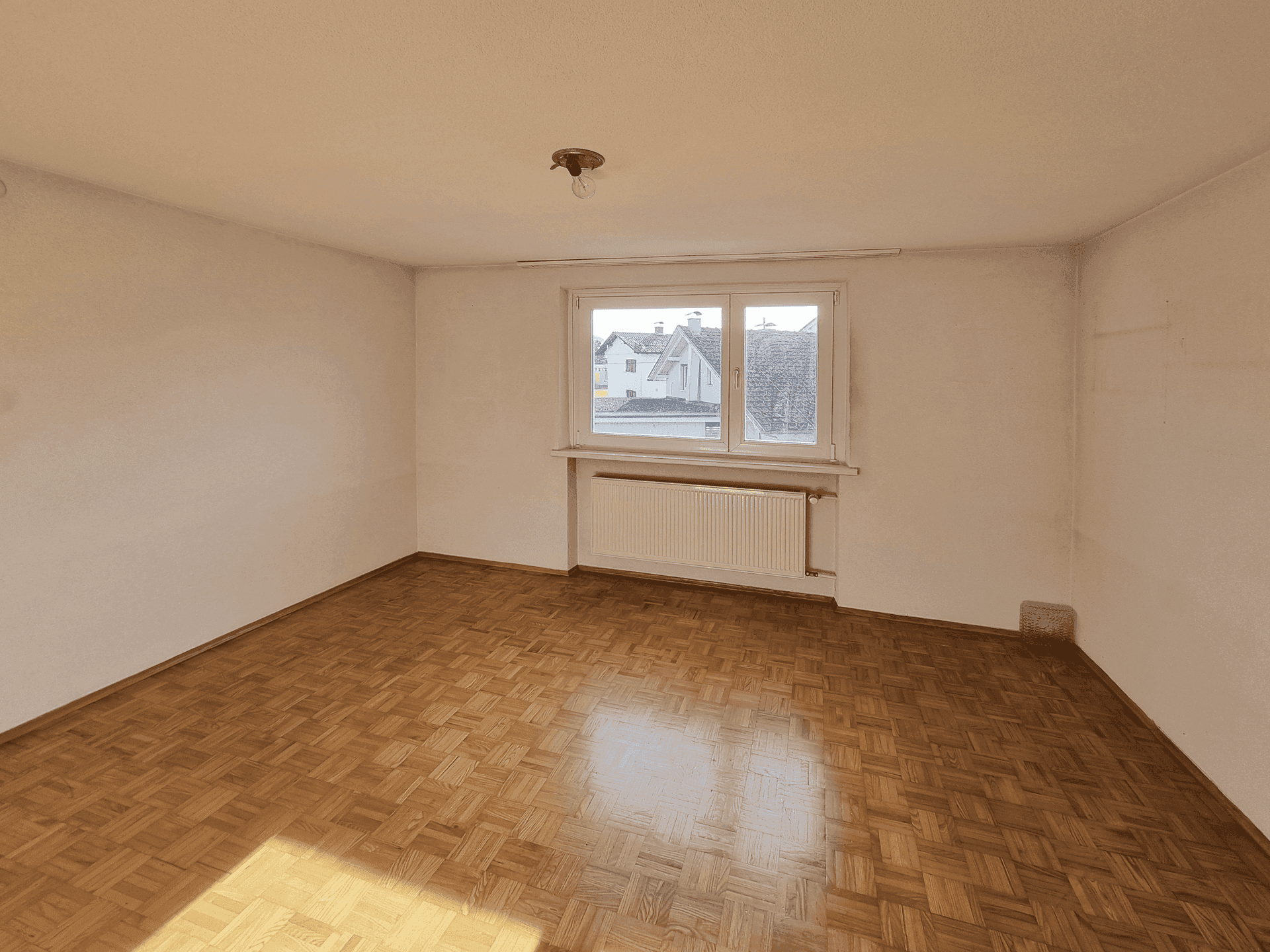 Helles Schlafzimmer mit Parkettboden und einem Fenster mit Blick auf die Umgebung.