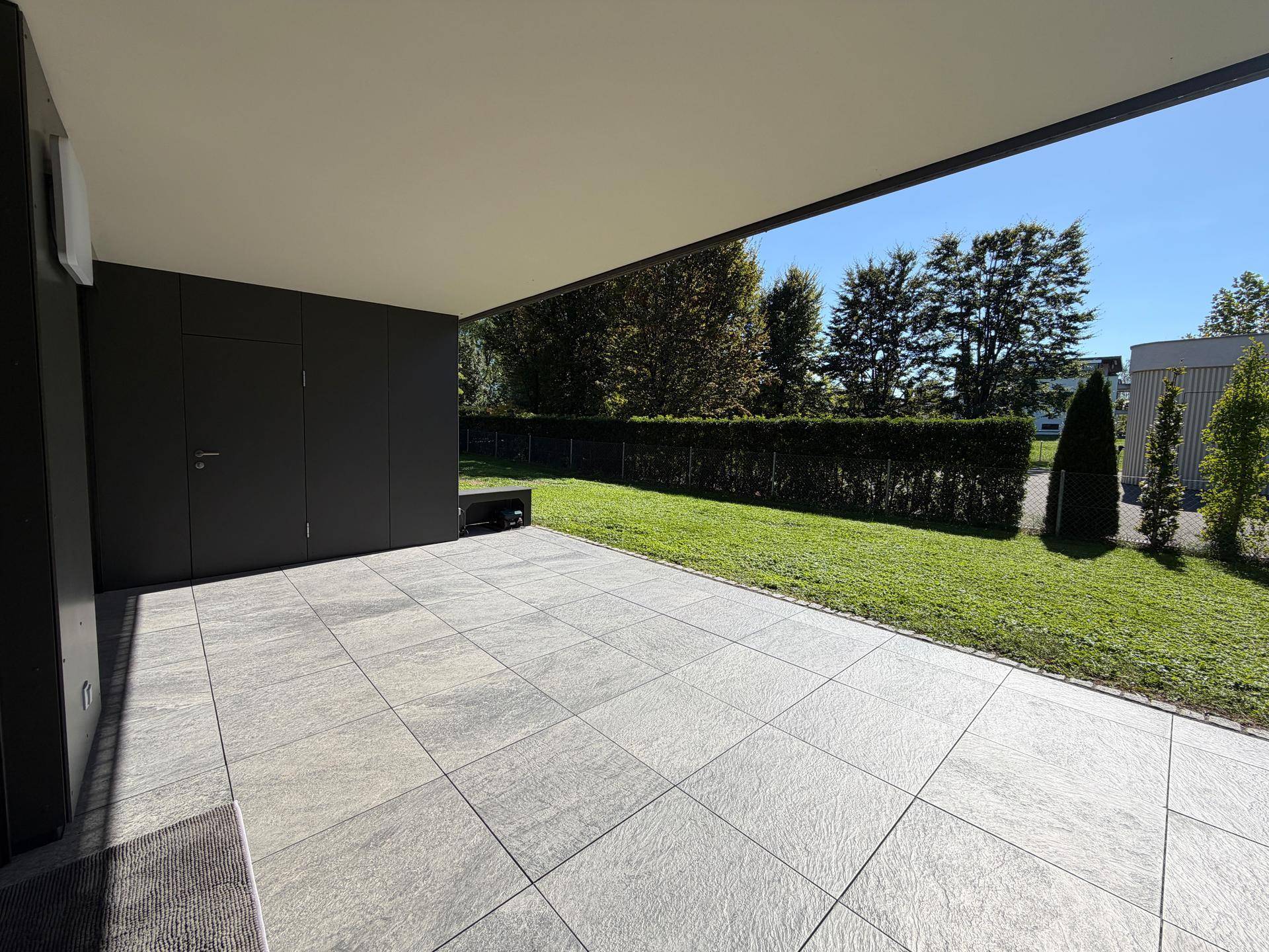 Überdachte Terrasse mit großformatigen Fliesen und Blick auf den gepflegten Garten.
