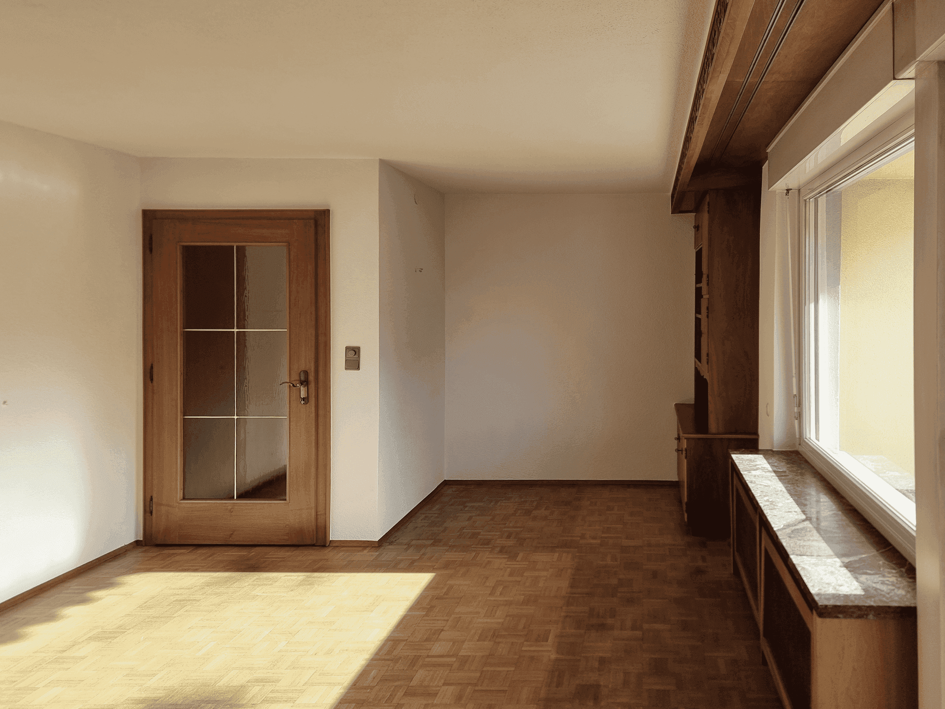 Geräumiges Wohnzimmer mit Parkettboden und viel Tageslicht durch große Fenster.